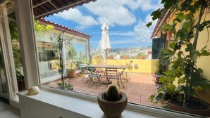 A view from a window overlooking a patio with a table and chairs, potted plants, and a distant view of a church and buildings. - Le terrazze di Chiaia is a charming penthouse with two large panoramic terraces (Napoli)