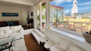 A living room with a white sofa, a glass coffee table, and a view of the patio with outdoor furniture and plants. - Le terrazze di Chiaia is a charming penthouse with two large panoramic terraces (Napoli)