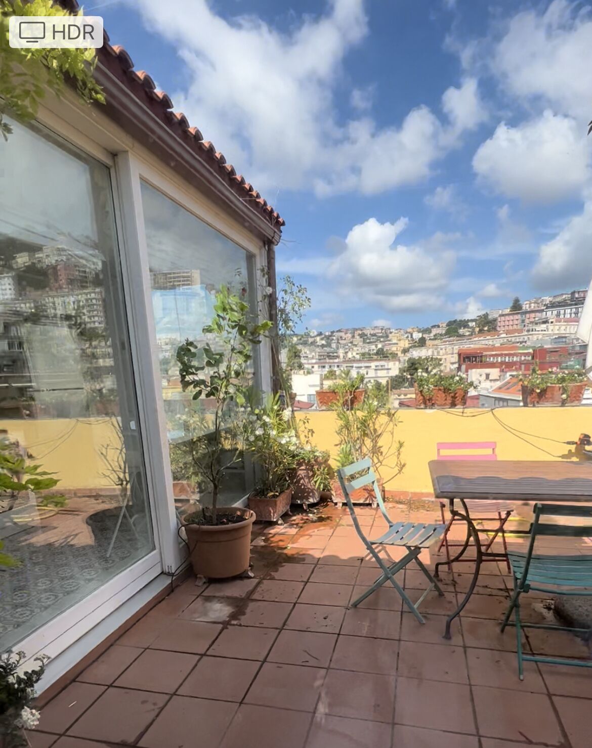 Eine Terrasse mit Topfpflanzen, einem Tisch und Stühlen.