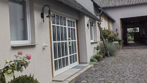 Une maison avec une allée pavée, une porte blanche dotée de panneaux de verre et un toit recouvert de tuiles.