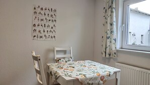 Un coin repas comprenant une table et des chaises, une fenêtre avec des rideaux et un mur orné d’une œuvre d’art à motifs.