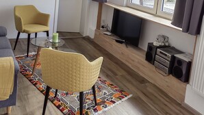 Un salon moderne comprenant un canapé, deux fauteuils, une table basse, un téléviseur et une fenêtre avec des rideaux.