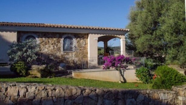A stone building with a tiled roof, a covered porch, and a stone wall in the foreground.