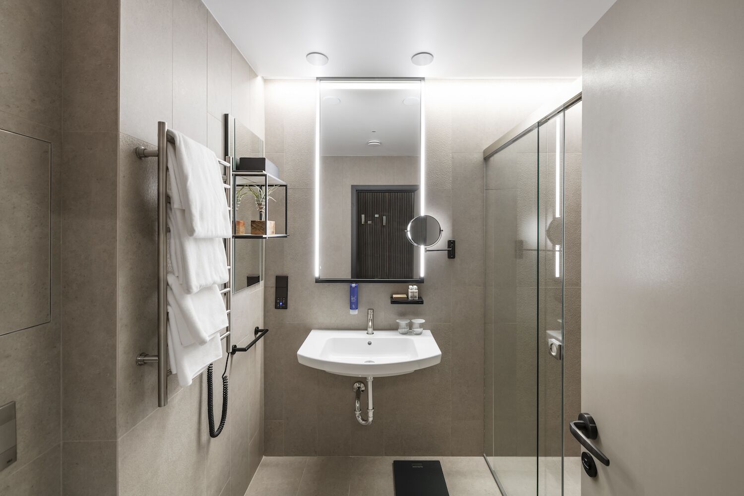 Un baño moderno con un lavamanos blanco, un espejo, un perchero para toallas y una cabina de ducha de cristal.