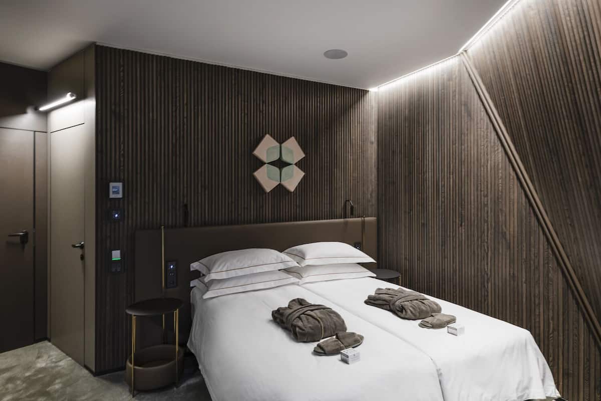 Ein modernes Hotelzimmer mit einem großen Bett, einem Nachttisch, einem kleinen Hocker und einer Wandleuchte.