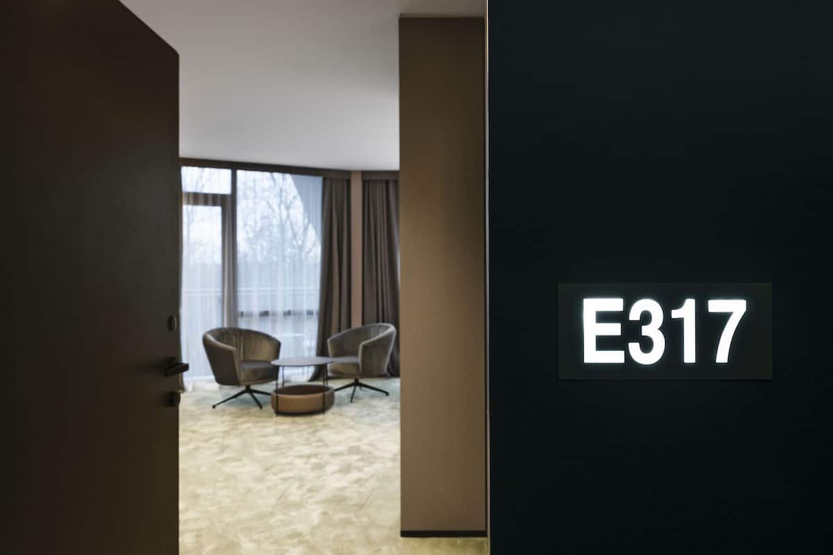 Ein modernes Hotelzimmer mit einem großen Fenster, zwei Sesseln, einem kleinen Tisch und einem Schild mit der Zimmernummer E317.