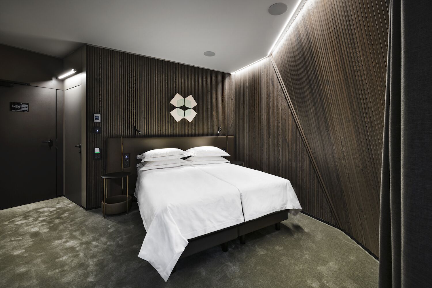 Una habitación de hotel moderna con una cama grande, un panel de control y una pared de paneles de madera.
