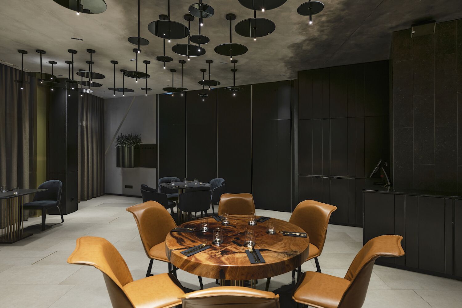A modern dining area with a round wooden table, leather chairs, and pendant lighting.