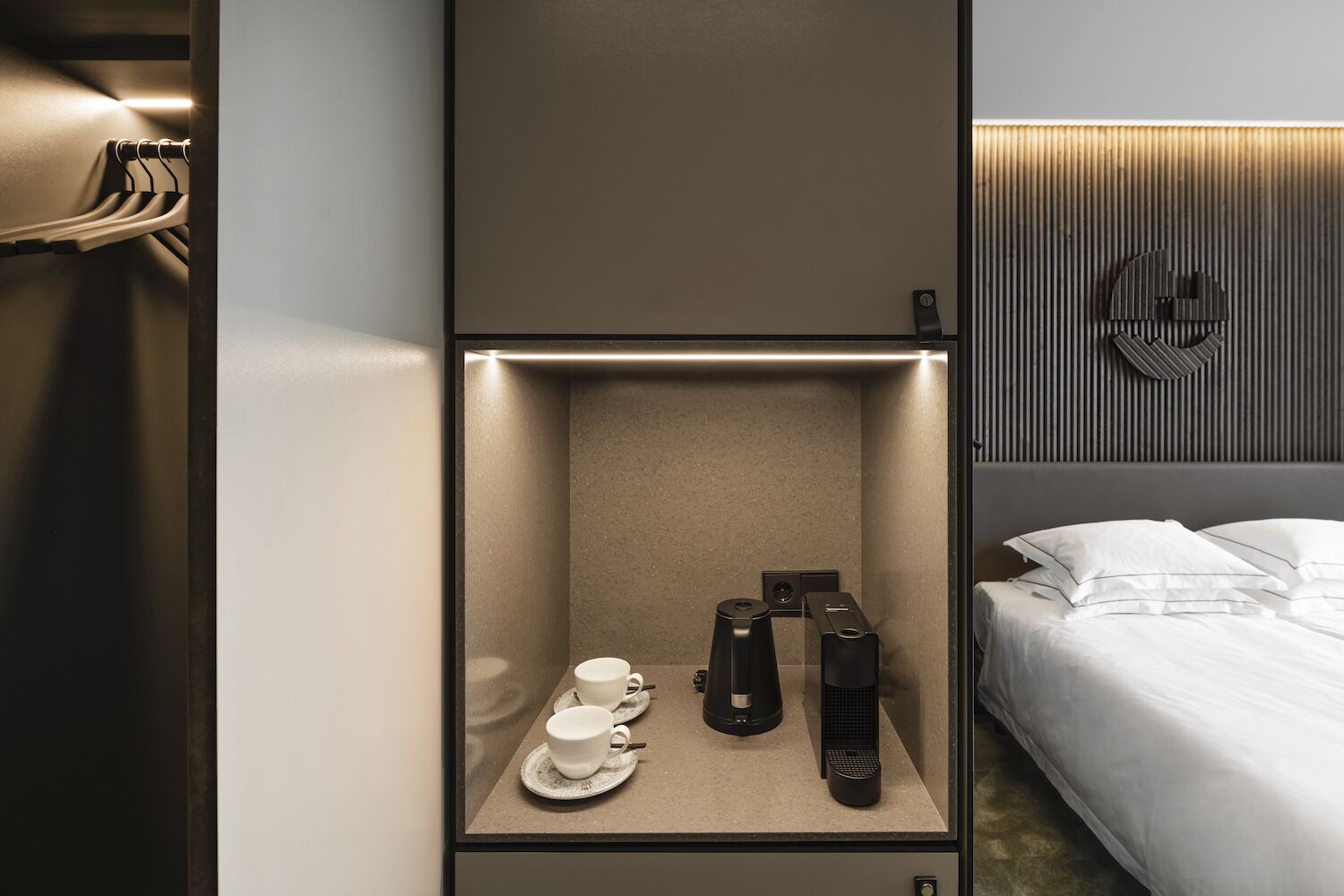 Una habitación de hotel con minibar, cama y lámpara fijada a la pared.