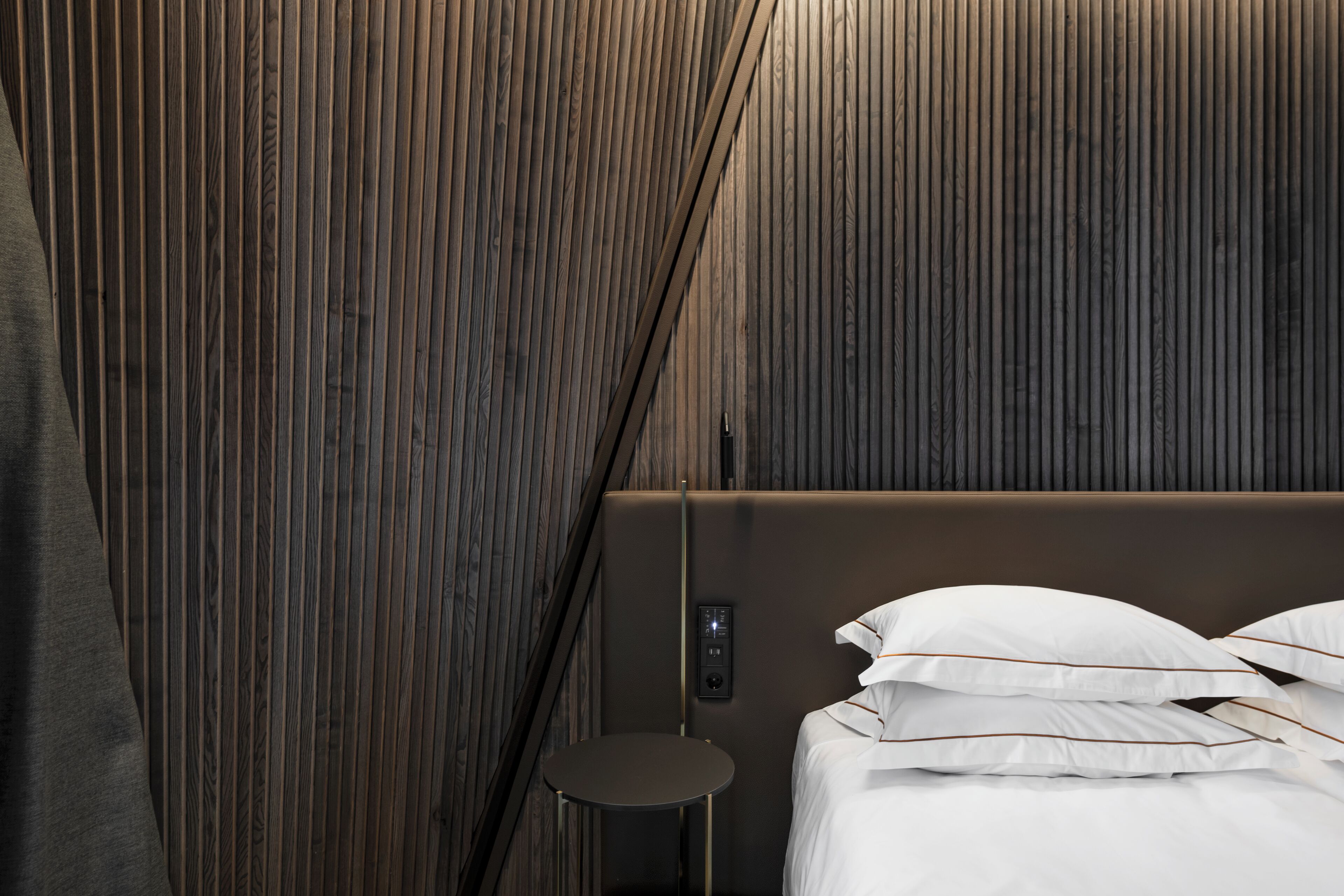 Un dormitorio moderno con una pared de paneles de madera, una cama con ropa de cama blanca y una pequeña mesa redonda.