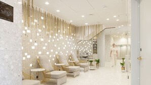 A modern lobby with a marble floor, seating area with armchairs and tables, a reception desk, and a staircase with a decorative wall. - MANA Sleep & SPA (Druskininkai)