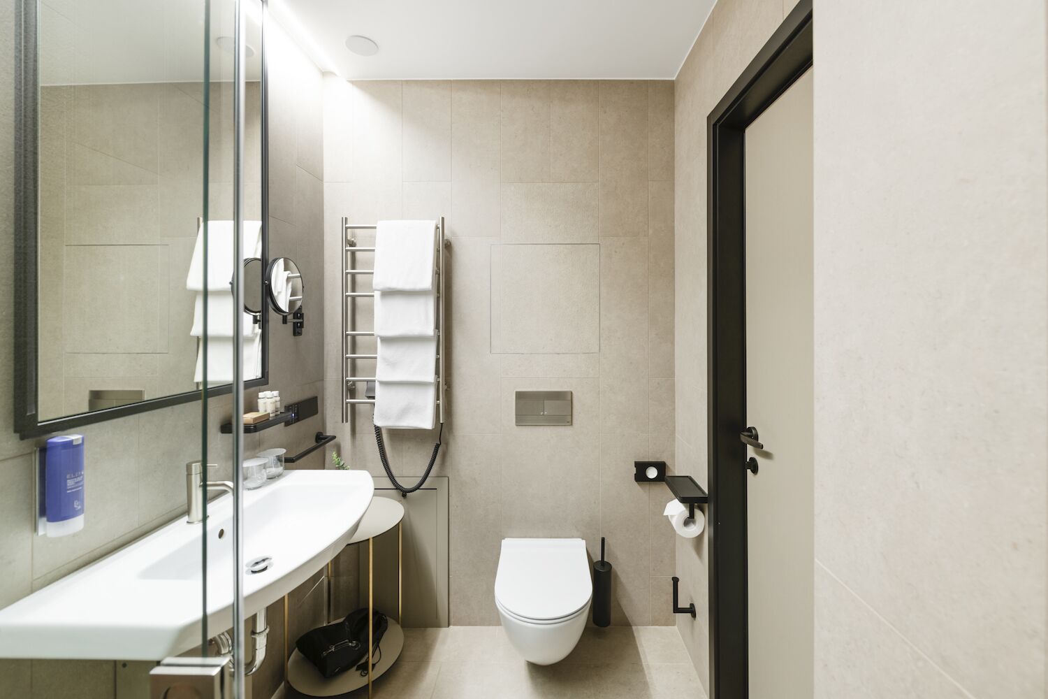 A modern bathroom with a white sink, mirror, towel rack, toilet, and a black door.