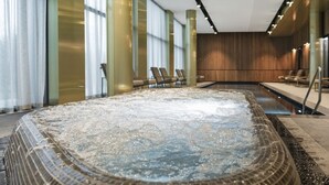 A large indoor hot tub with a tiled interior, surrounded by lounge chairs and a wooden wall. - MANA Sleep & SPA (Druskininkai)