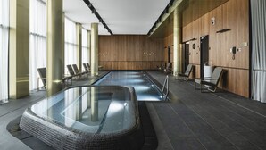 A modern indoor swimming pool with a glass enclosure, wooden panel walls, and seating areas with chairs. - MANA Sleep & SPA (Druskininkai)