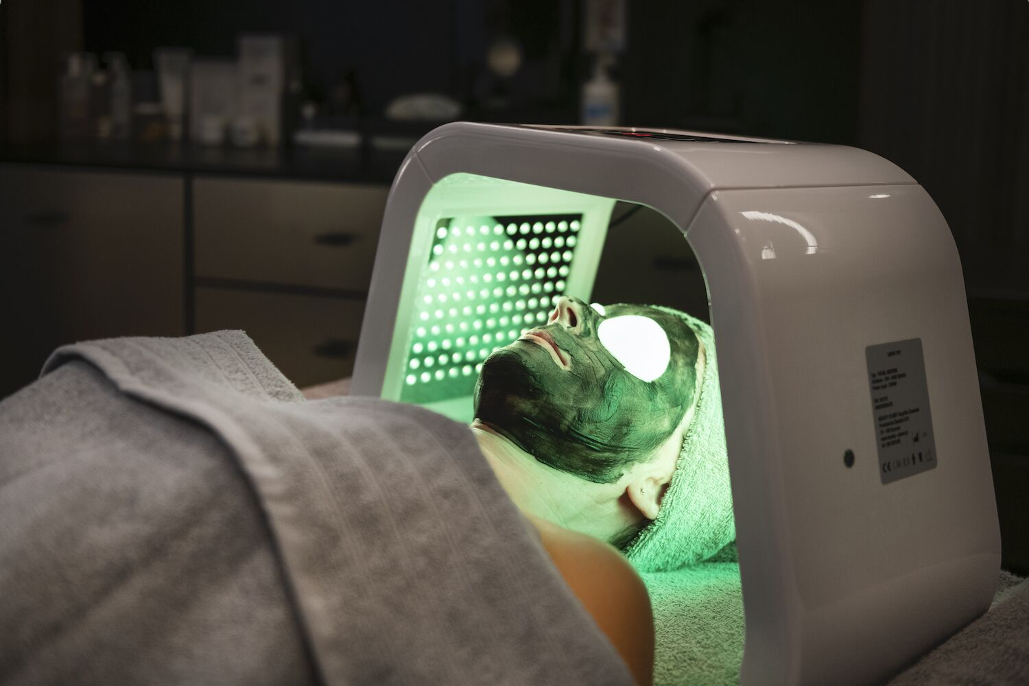 A person lying down with a green light therapy device on their head.