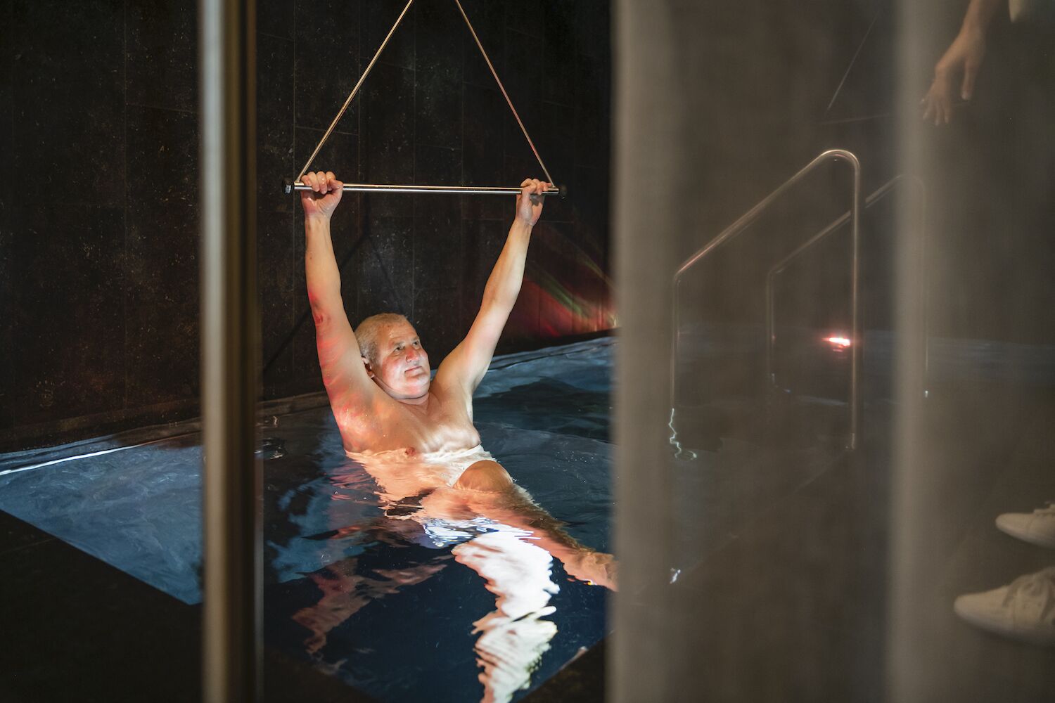 A person performing an aerial yoga pose in a dimly lit room with a reflective surface.