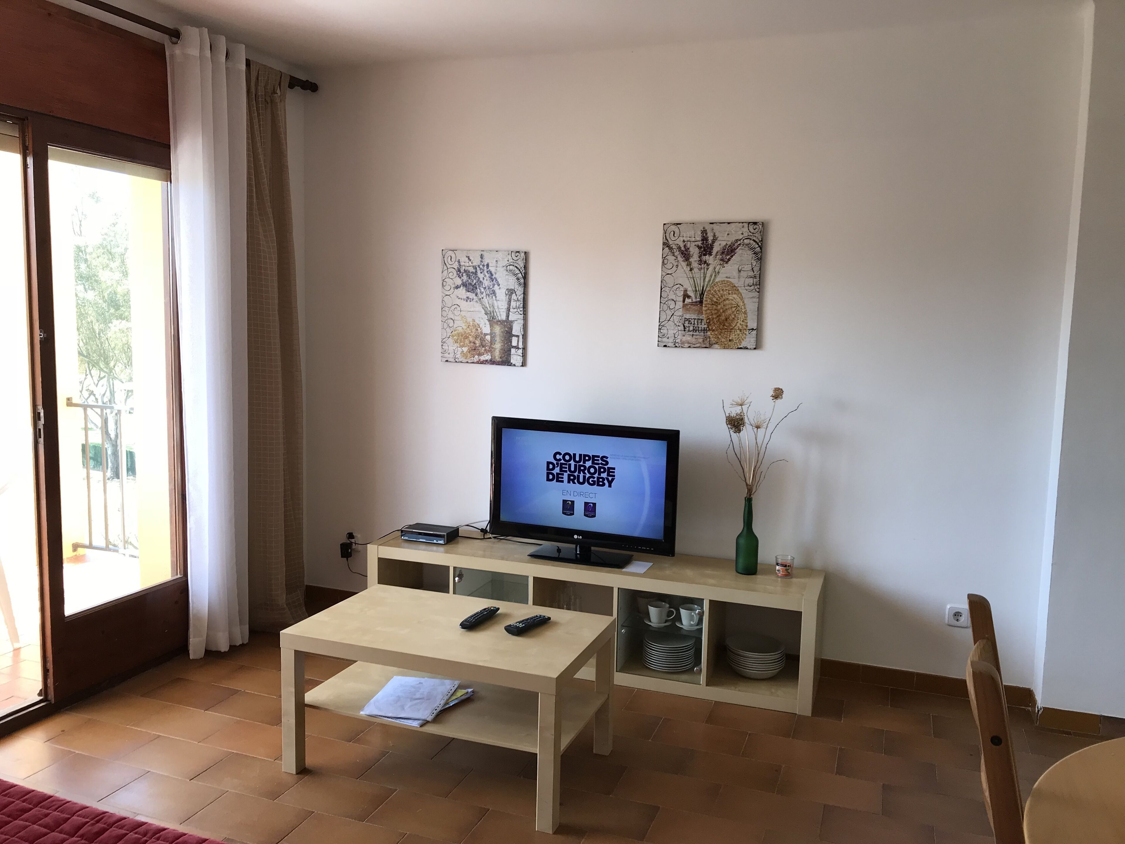 Un salon avec un téléviseur, une table basse et un buffet contenant de la vaisselle.