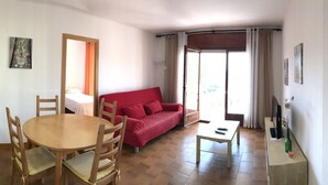 A living room with a red sofa, a wooden dining table, and a TV. - Apartment l'Estartit beach (Torroella de Montgrí)