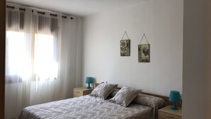 A bedroom with a bed, two bedside tables, a window with curtains, and two wall-mounted lamps. - Apartment l'Estartit beach (Torroella de Montgrí)