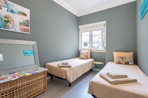 Un dormitorio con dos camas, una ventana y una estantería de pared con libros.