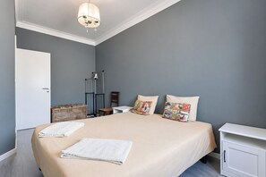 Une chambre à coucher comprenant un lit, deux oreillers, une table de chevet, une chaise, une armoire et un luminaire suspendu.