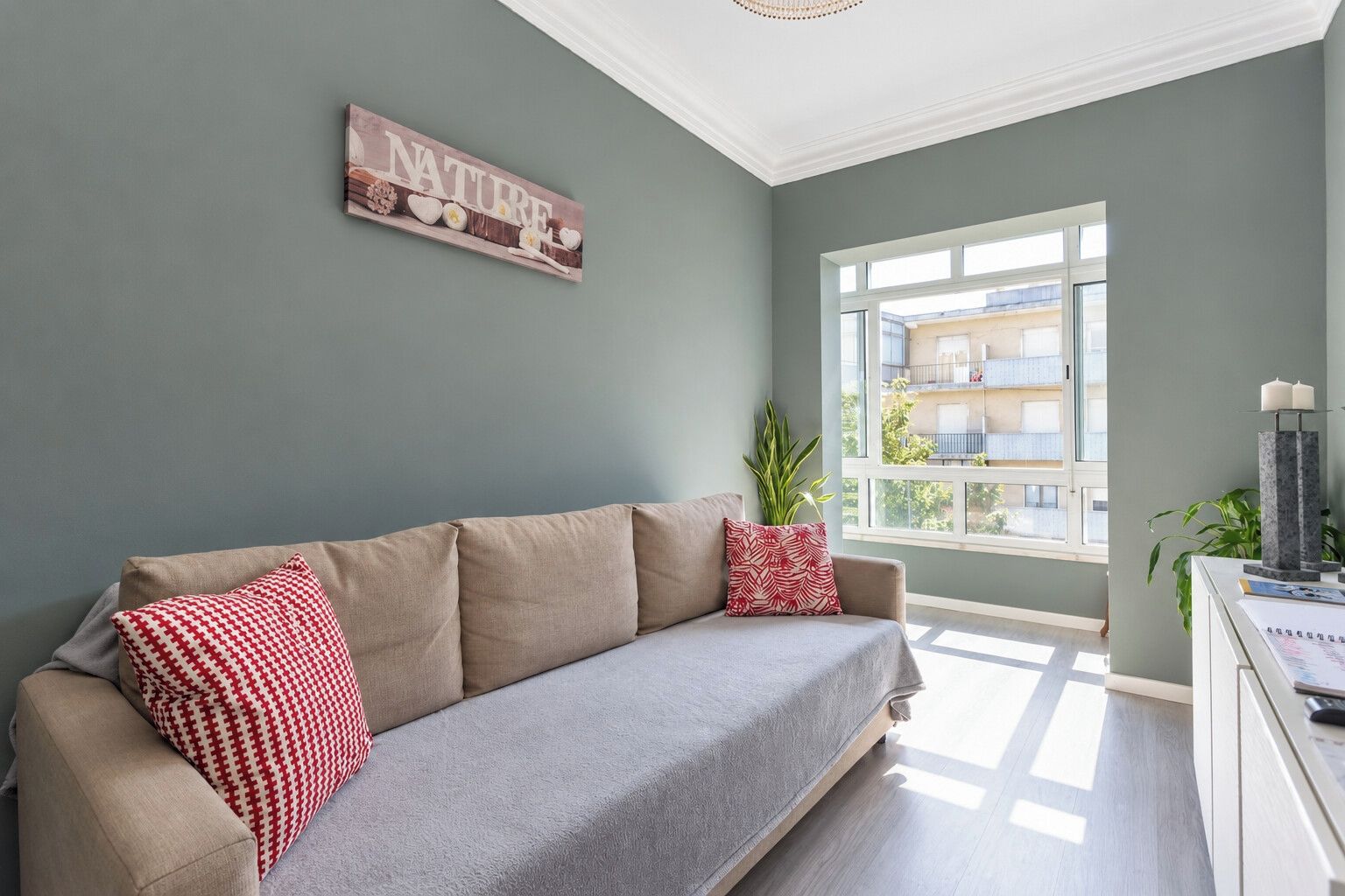 A living room with a sofa, pillows, a wall sign, a window, and a plant.