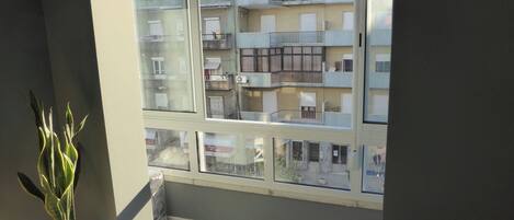 A balcony with a view of a multi-story building, a potted plant, and a window with blinds.