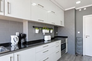 Una cocina moderna con armarios blancos, encimera negra, cafetera, tostadora y macetas colgantes.