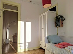A bedroom with a bed, a wardrobe, a hanging plant, and a door leading to another room.