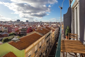 A balcony with a view of a cityscape, including buildings with red-tiled roofs and a clear sky.