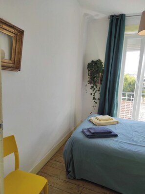Ein Zimmer mit einem Bett, einem Sessel, einer hängenden Pflanze und einem Fenster mit Vorhängen.