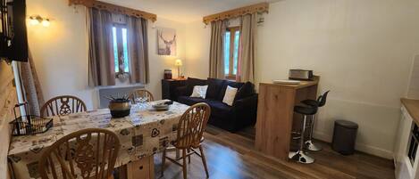 A cozy living area with a dining table, chairs, a sofa, and a TV.