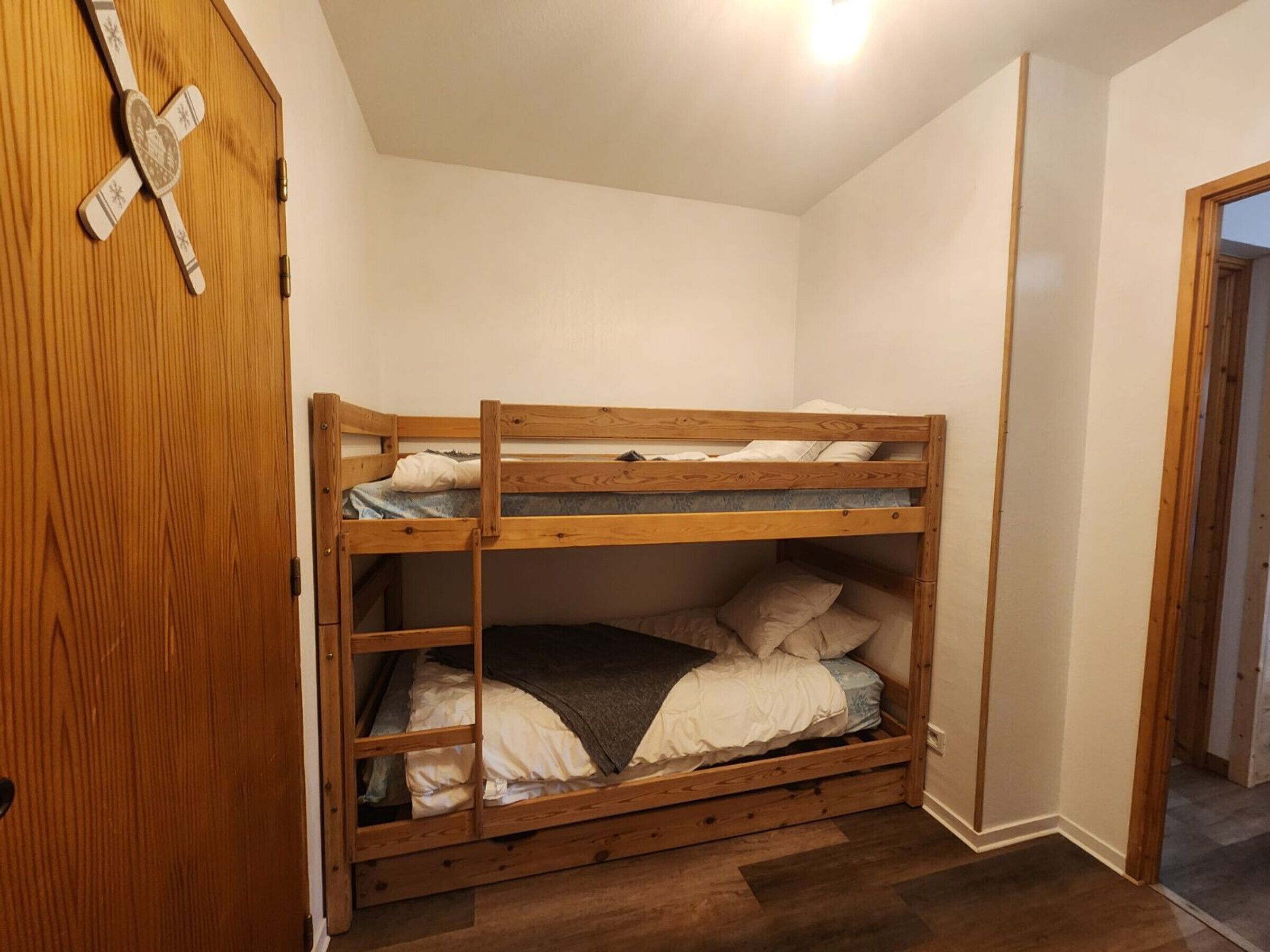 A bunk bed in a room with wooden flooring and a wooden door.
