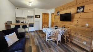 A compact living space with a kitchenette, dining area, and a TV mounted on a wooden wall. - 2-room apartment with balcony in Samoëns, parking included (Samoëns)