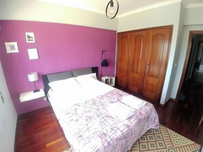 A bedroom with a bed, a nightstand, a lamp, a wardrobe, and a wall with pictures.