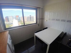 A kitchen with a window, white tiled walls, and a white table.