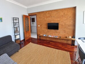 Een woonkamer met een bank, een salontafel, een televisie die aan een bakstenen muur is bevestigd en een boekenkast.