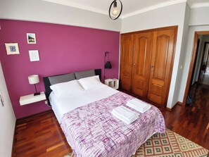 Een slaapkamer met een bed, een kledingkast, een nachtkastje en een wand met afbeeldingen.