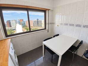 Een compacte keuken met een eettafel en stoelen, een raam met uitzicht over de stad, en een wasmachine.