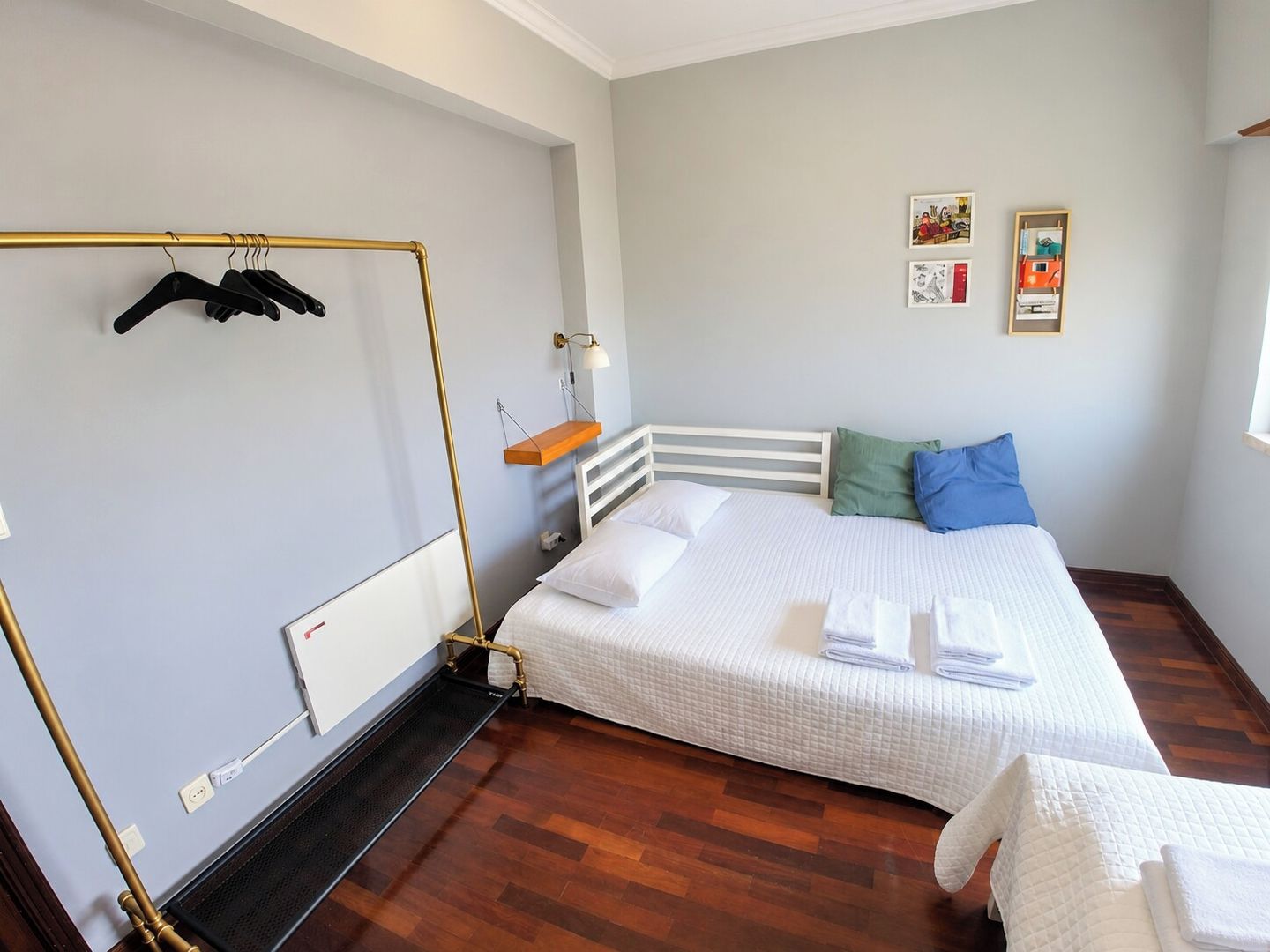 Un dormitorio con cama, mesita de noche, lámpara, radiador y estante en la pared.