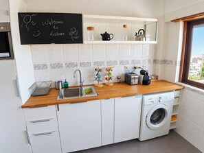 Une cuisine compacte équipée d’un évier, d’un grille-pain, d’une bouilloire et d’un lave-linge.