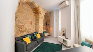 Un soggiorno moderno con una parete in pietra, un divano grigio con cuscini gialli, un tappeto verde e un tavolino bianco.