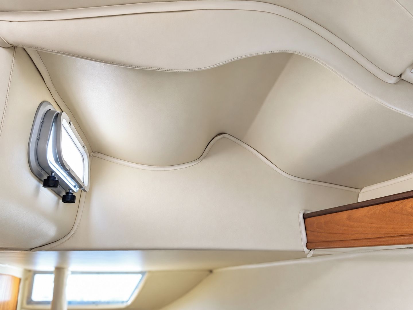 Onderdeel van het interieur van een voertuig met een gebogen leren stoel en een bedieningspaneel met twee zwarte knoppen.