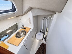 Een kleine keuken met een roestvrijstalen spoelbak, een houten werkblad en een wit toilet met waterreservoir.