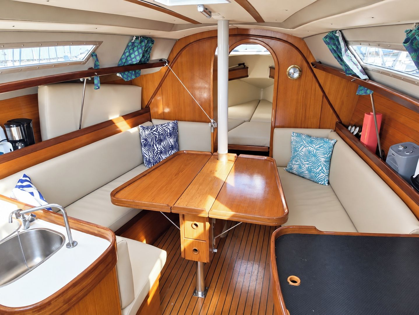 A compact boat interior with a dining area, seating, a small sink, and a window.