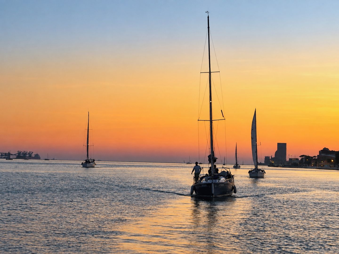 A sunset over a calm body of water with sailboats.