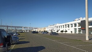 Een parkeerplaats met meerdere auto's, een brug op de achtergrond en een modern gebouw met schotelantennes.