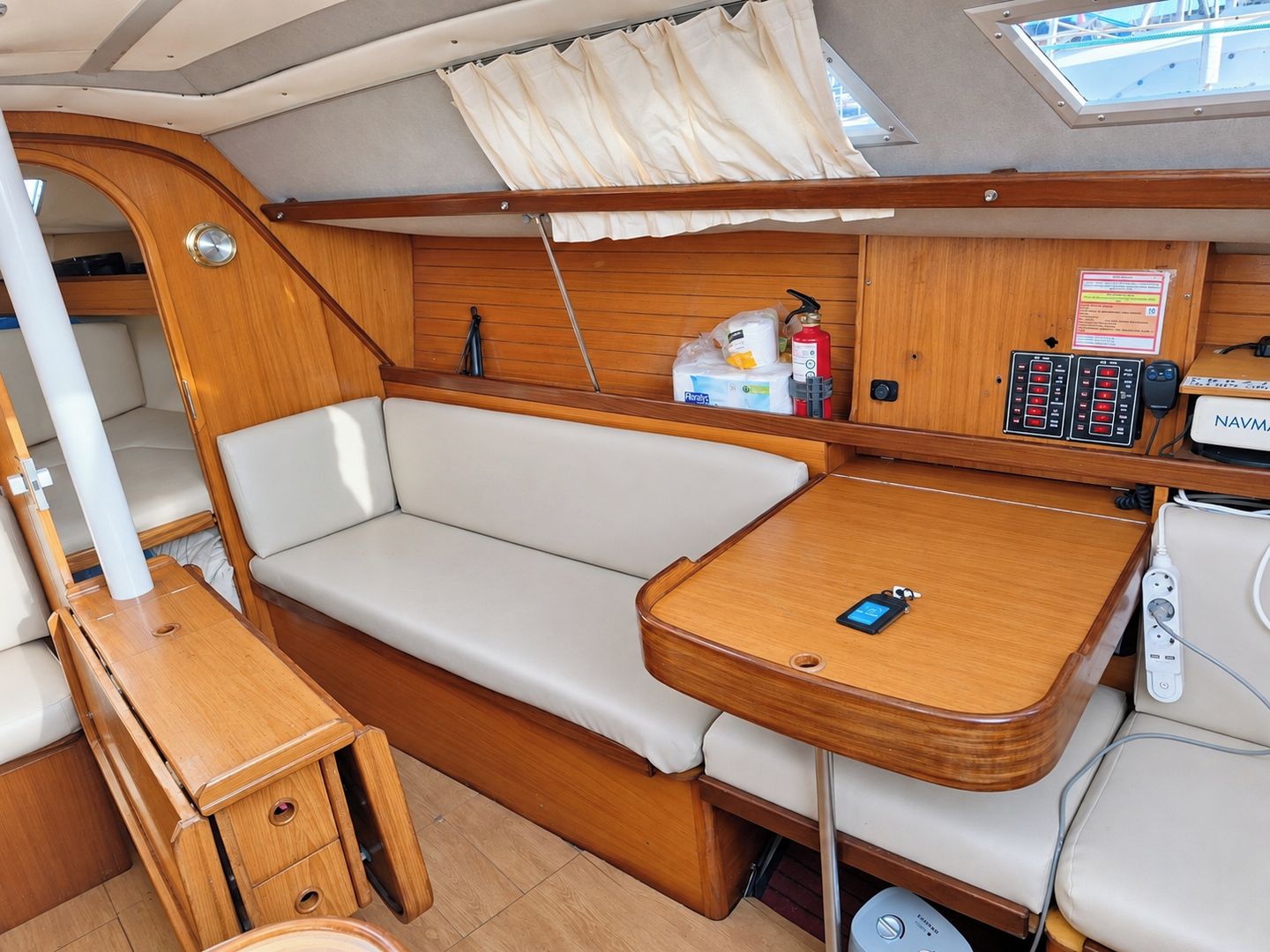 A compact boat interior with a cushioned seating area, a small wooden table, and a control panel with various buttons and a display.