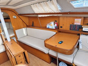 Un intérieur de bateau compact comprenant un coin salon avec des sièges rembourrés, une petite table en bois et un panneau de commande doté de divers boutons et d’un écran.
