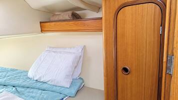 Un letto con copriletto azzurro trapuntato e un cuscino bianco, un armadio in legno con maniglia rotonda e uno scaffale sopra il letto.
